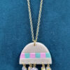 Inverted-bowl-shaped pendant on a yellow brass chain in white pearl clay with a row of alternating squares in pink and green along the bottom edge, dangling five square lampwork beads in pale colours.