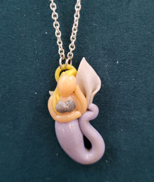 MermaidAstaClose A blonde, light-skinned mermaid with a grey-blue tail and seashell bra, her head resting against her hand and that arm supported by her upraised tail